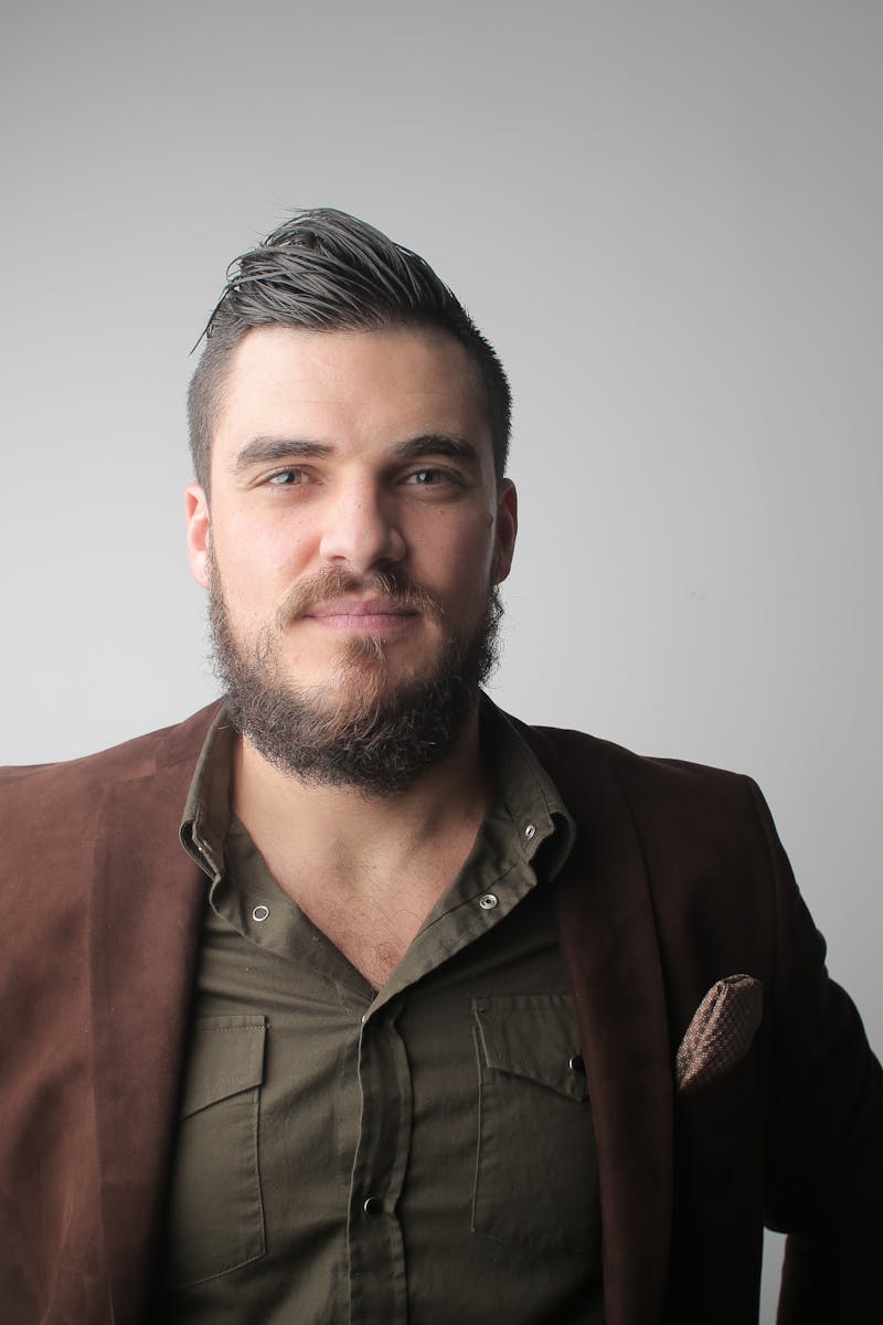 Close-up portrait of a bearded man in a stylish jacket, photographed in a studio setting.